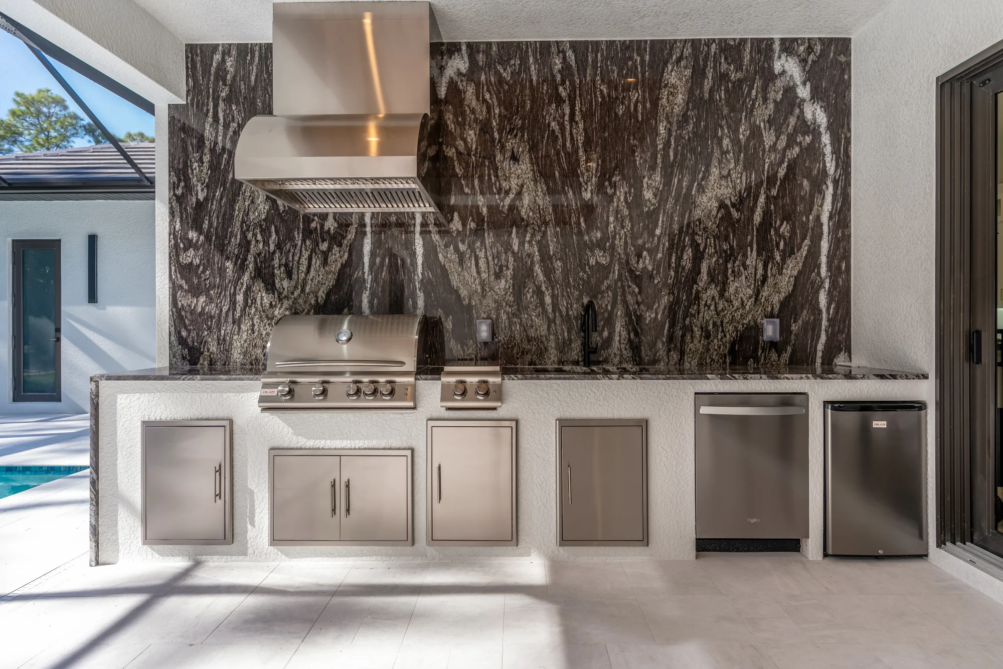 Outdoor kitchen with stainless steel appliances and bar seating in Sunset Golf modern golf estate home at 524 22nd Ave NW, Naples FL by XL Homes custom home builder