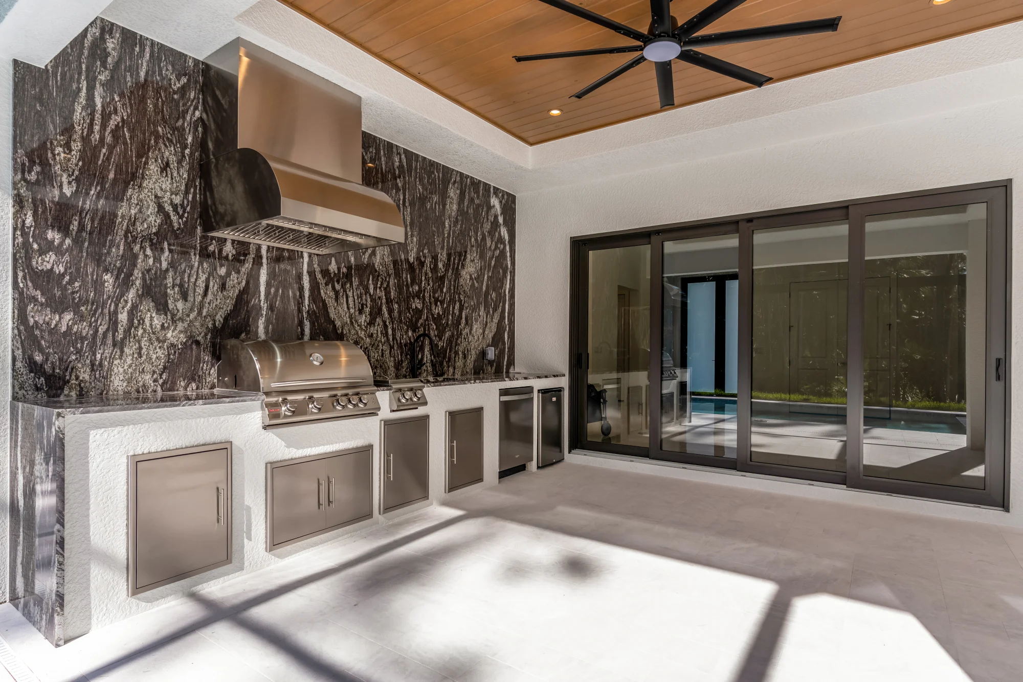 Outdoor kitchen with stainless steel appliances and bar seating in Sunset Golf modern golf estate home at 524 22nd Ave NW, Naples FL by XL Homes custom home builder