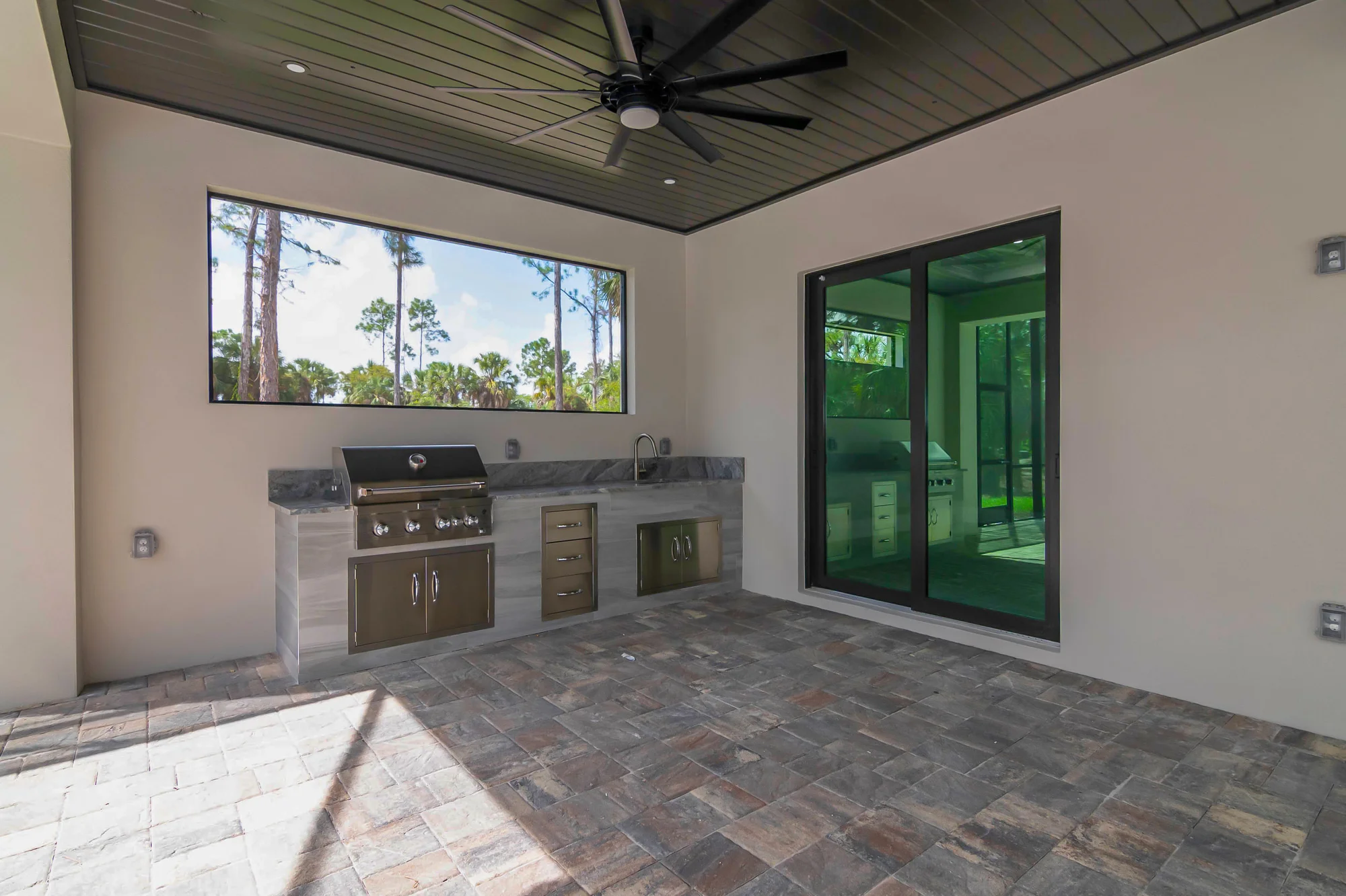 Outdoor kitchen with stainless steel appliances and bar seating in The Oasis coastal contemporary home at 760 15th St SW, Naples FL by XL Homes custom home builder